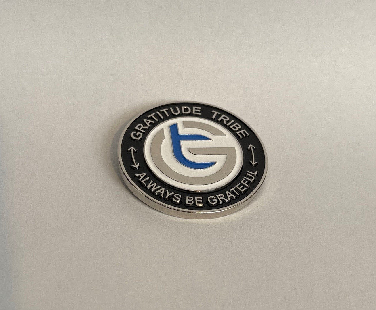 Circular metal badge with 'Gratitude Tribe' logo and text on a light gray background, coin, front,